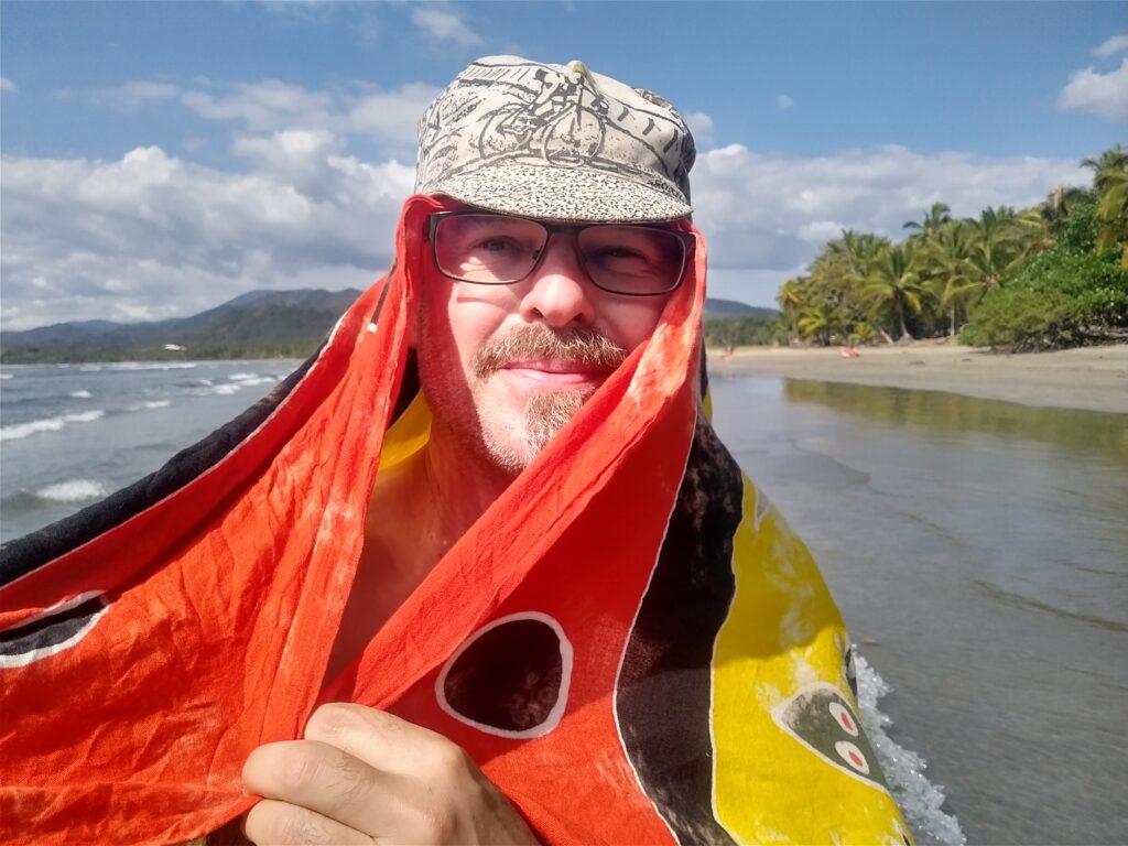 Alec Hager mit Fahrradcap und buntem Tuch am Strand von Costa Rica