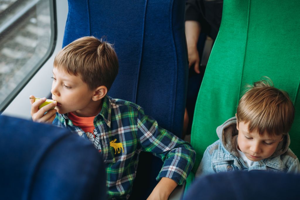 Zwei Kinder (männlich gelesen, geschätzt zwischen 8 und 10 Jahr alt) auf Sitzplätzen im Zug