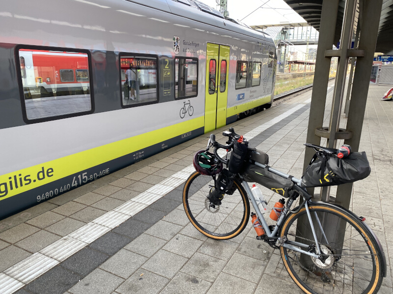 Bereit für die Fahrradmitnahme im Zug. Ein bepacktes Fahrrad am Bahnsteig. Im Hintergrund ein Regionalzug