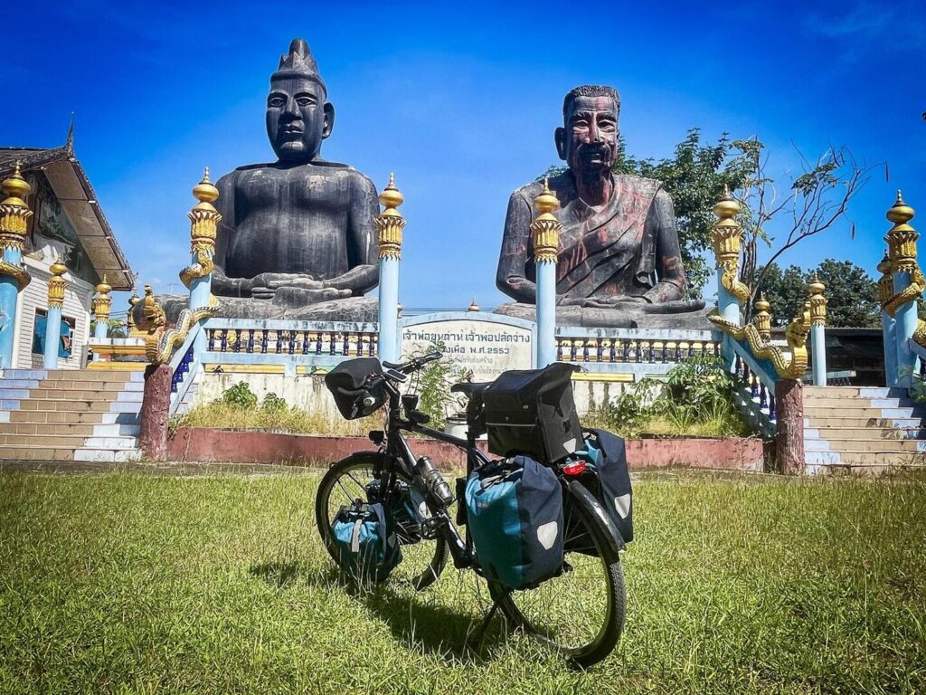 zwei Statuen an einem thailändischen Tempel. Oliver Baiers Reiserad im Vordergrund