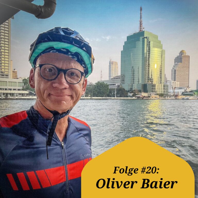 Oliver Baier mit Helm und Fahrradtrikot bekleidet vor der Kulisse von Bankok